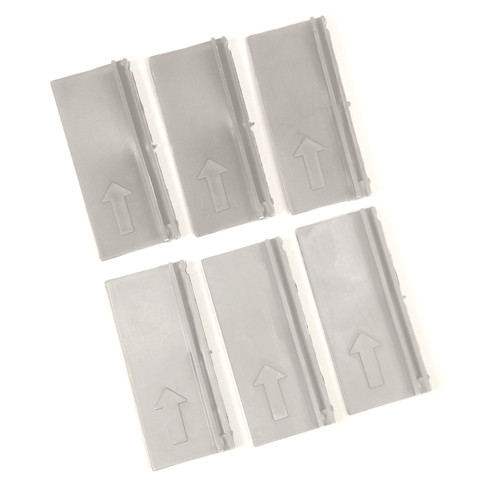 Six gray plastic pieces with upward arrows laid out in a loose grid pattern, likely spacers or tabs used in assembly.