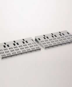 Two gray perforated plastic panels with a grid of small rectangular cutouts, laid angled on a white surface.