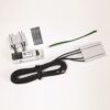 Electronic hardware kit laid out on a white surface: a gray module with a black connector, a second gray housing, a long coiled black cable, a small label card, and a green/black two‑conductor ribbon cable.
