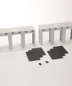 Two gray scale-model bridge-like frames with four legs and a ribbed top, plus dark foam sheets and tiny screws on a white surface (model kit parts).