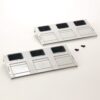 Two white plastic mounting panels with three square openings each and small sliding covers, laid on a white surface with two screws nearby.