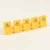 Six yellow safety tiles with high-voltage warning symbols arranged in a row (toy-like blocks).